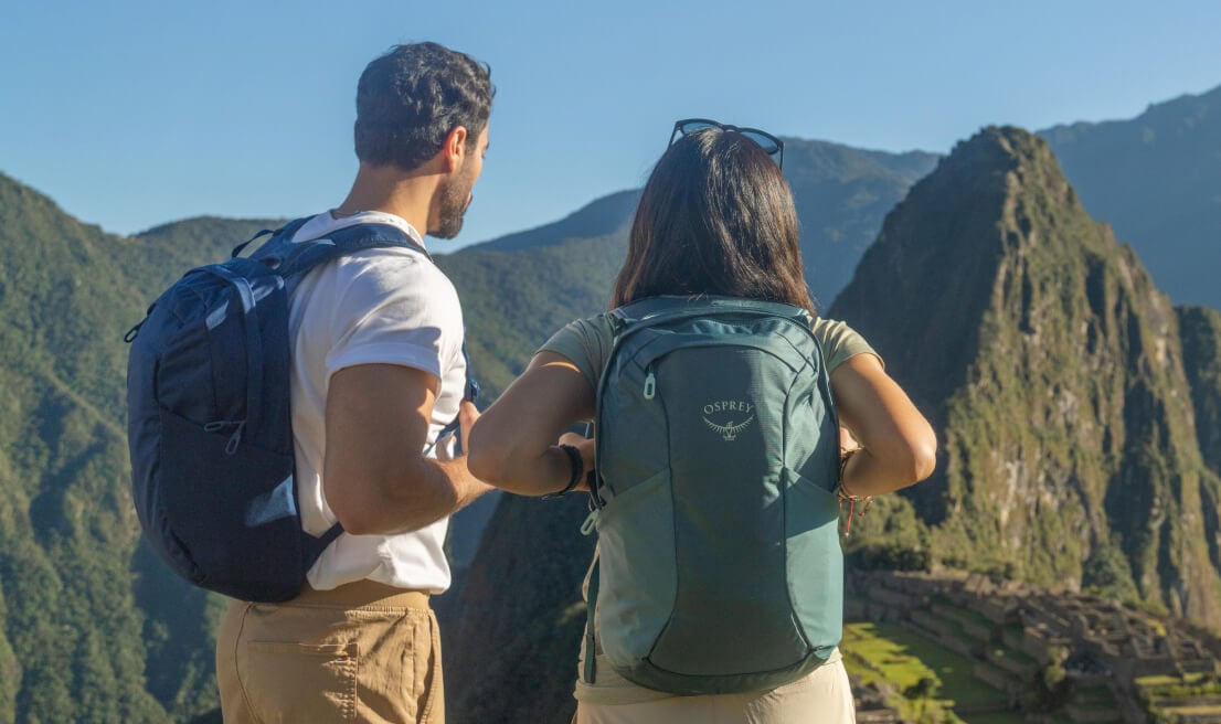 Travelers wearing Osprey Farpoint and Fairview daypacks overlooking mountain landscape