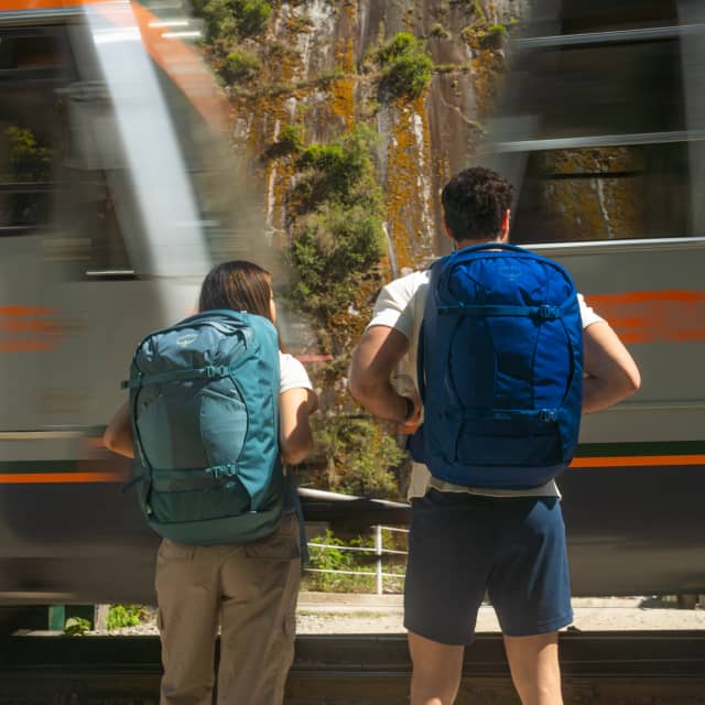 Travelers with Osprey backpacks waiting for train to pass.