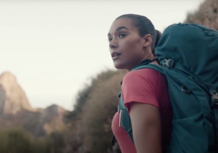 Farbfoto einer blonden Frau in lila Jacke und marineblauem und grauem Osprey-Rucksack vor blauem Himmel. Eine orangefarbene Isomatte und eine schmale gelbe Tasche sind außen am Boden des Rucksacks festgeschnallt. Das Foto ist mit schwarzem Filzstift signiert und trägt die Aufschrift: „A great pack - '100 miles' Wind Rivers, Big Sandy to Green River. Fran Schmuch August 1992“