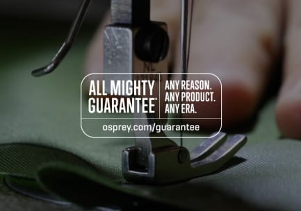 Das Logo der All Mighty Guarantee über einem unscharfen Foto von einer Nähmaschine, einer Hand und einem Stoff. Auf dem Logo steht: „Any Reason. Any Product. Any Era. osprey.mom/guarantee”