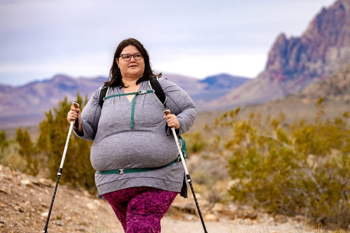A woman wearing a gray and purple hiking with hiking poles