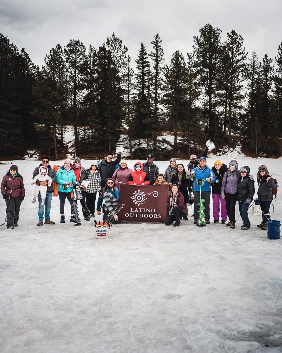A group of people outside in the snow, gathered around a Latino Outdoors flag