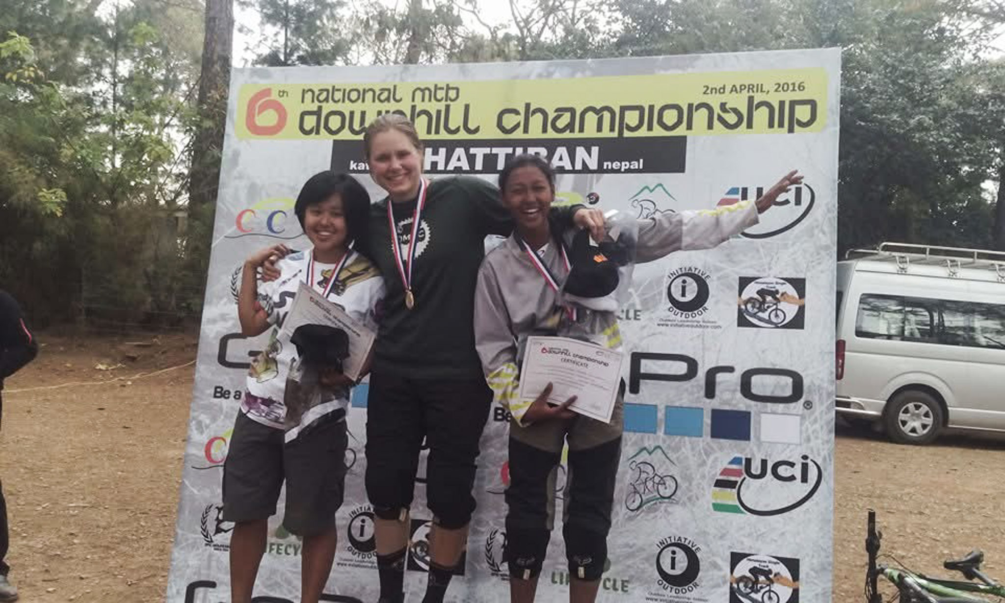 Three people stand on a podium showing off their certificates and medals.