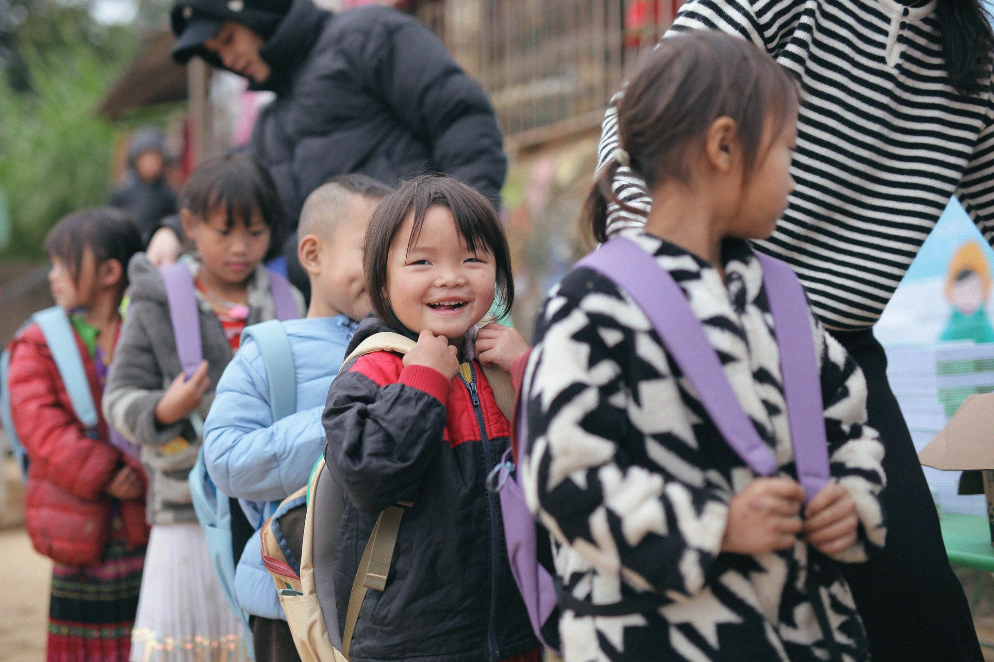 Kids line up wearing backpacks, one child smiles at the camera.