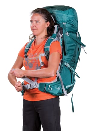 A woman in an orange graphic t-shirt wearing a teal backpacking pack over her shoulders is tightening the hipbelt&rsquo;s nylon
adjuster strap.