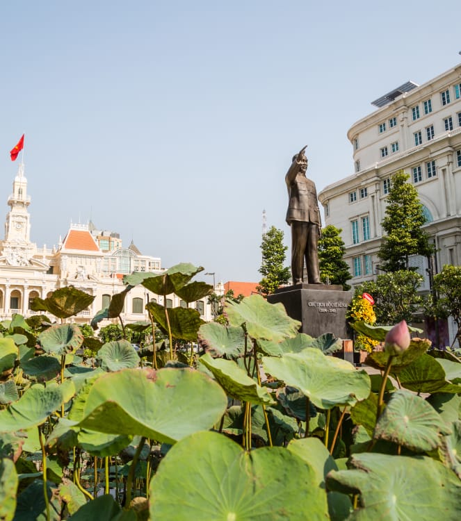 Lotus leaves and buds in the foreground and the Ho Chi Minh Statue in front of Saigon City Hall in Ho Chi Minh City, Vietnam.