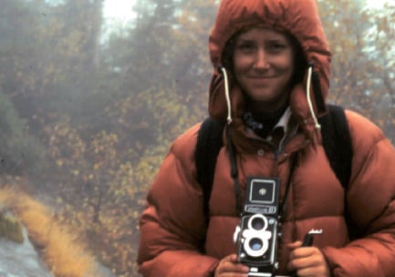 A woman poses in nature with a vintage camera.